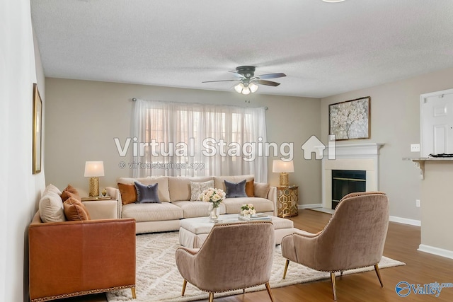 living area with a fireplace with flush hearth, a ceiling fan, a textured ceiling, wood finished floors, and baseboards