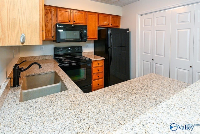 kitchen with light stone countertops, black appliances, brown cabinets, and a sink