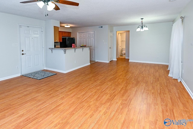 unfurnished living room featuring baseboards, light wood-style flooring, a textured ceiling, and ceiling fan with notable chandelier