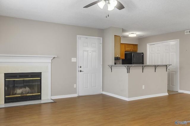 kitchen with light wood-style flooring, a kitchen bar, freestanding refrigerator, brown cabinetry, and a glass covered fireplace