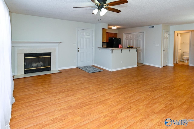 unfurnished living room with light wood-type flooring, a ceiling fan, visible vents, and a textured ceiling