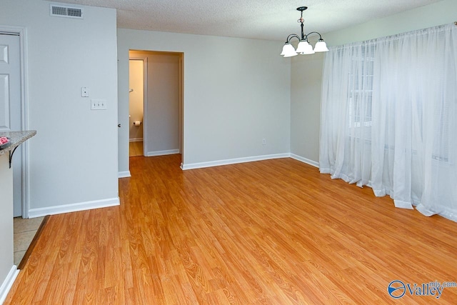 unfurnished dining area featuring baseboards, a textured ceiling, visible vents, and light wood-style floors