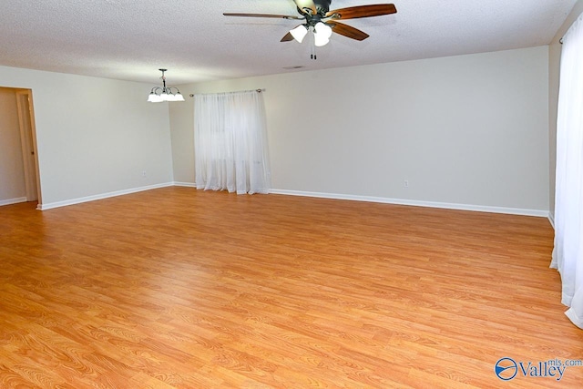 empty room with light wood-type flooring, a textured ceiling, baseboards, and ceiling fan with notable chandelier