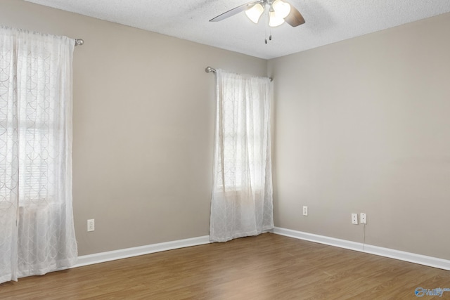 spare room with ceiling fan, a textured ceiling, baseboards, and wood finished floors