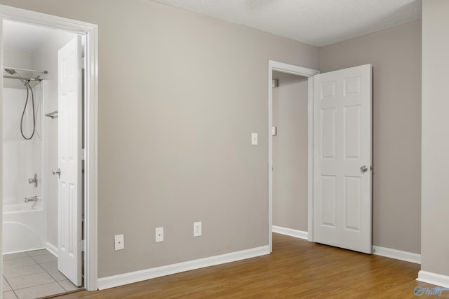 unfurnished bedroom featuring ensuite bath, a textured ceiling, baseboards, and wood finished floors