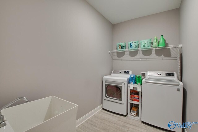 laundry area featuring washing machine and dryer, sink, and light hardwood / wood-style floors