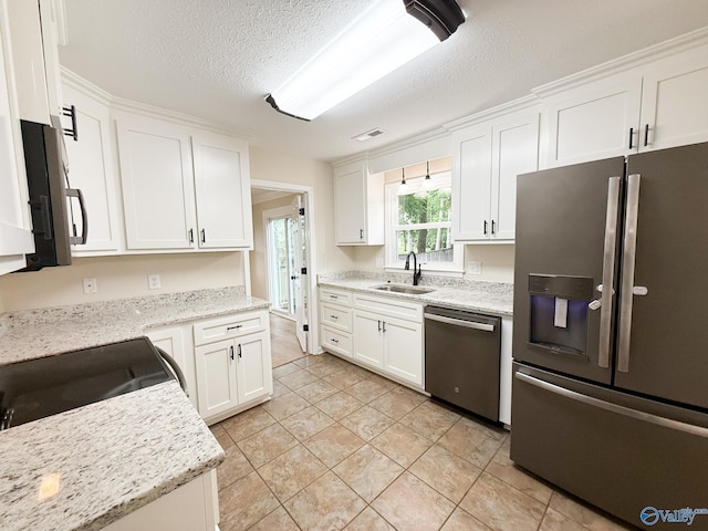 kitchen featuring appliances with stainless steel finishes, a sink, white cabinets, a textured ceiling, and light stone countertops