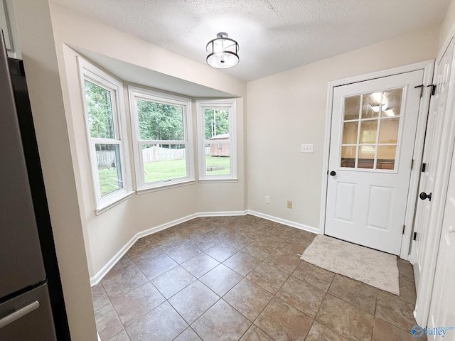 doorway to outside with plenty of natural light, a textured ceiling, baseboards, and tile patterned flooring