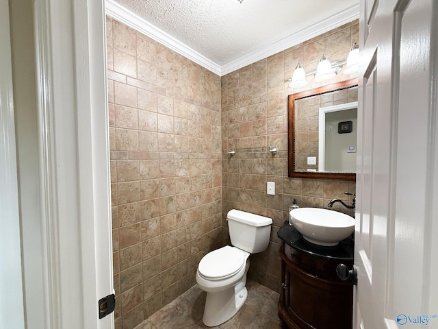 half bathroom featuring crown molding, toilet, a textured ceiling, vanity, and tile walls