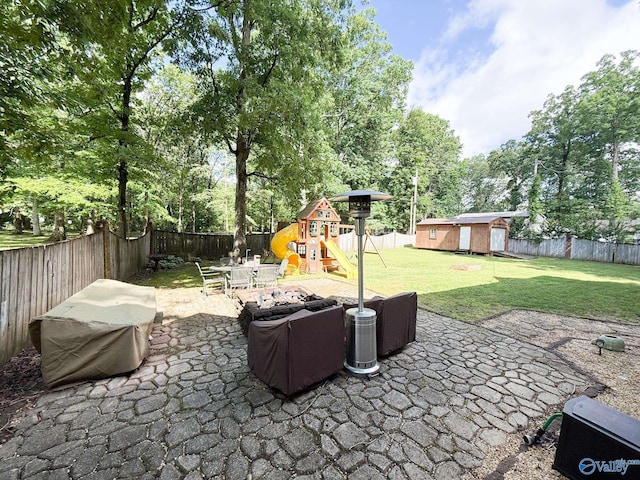 view of patio featuring a playground, an outdoor structure, view of wooded area, and a storage unit