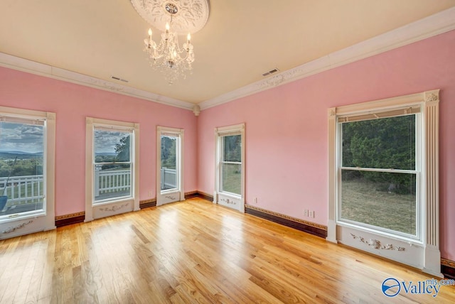 spare room with light wood-type flooring, crown molding, and a chandelier