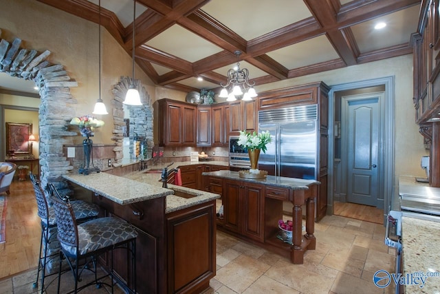 kitchen with decorative light fixtures, kitchen peninsula, stainless steel built in fridge, and light stone counters