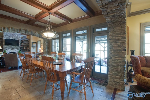 dining space with ornate columns, beamed ceiling, ornamental molding, coffered ceiling, and a stone fireplace