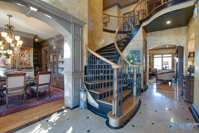 staircase with a high ceiling, decorative columns, an inviting chandelier, and ornamental molding