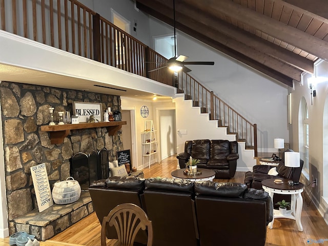 living area featuring stairs, a fireplace, wood finished floors, and beam ceiling