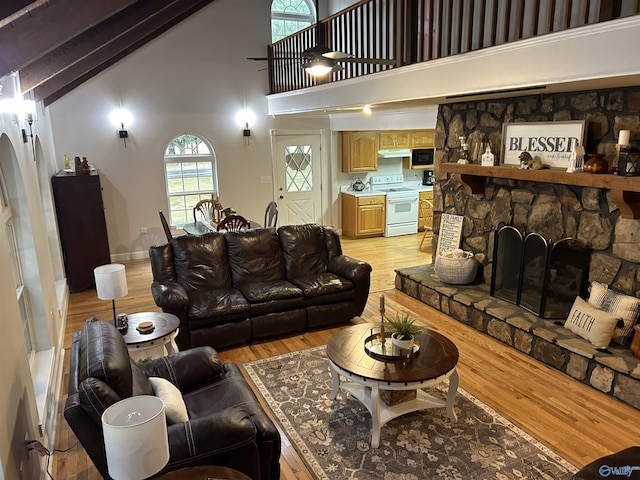 living area featuring high vaulted ceiling, a stone fireplace, and light wood-style floors