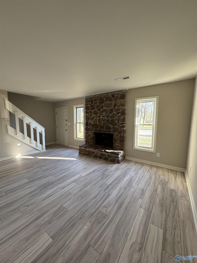 unfurnished living room with light hardwood / wood-style floors and a stone fireplace