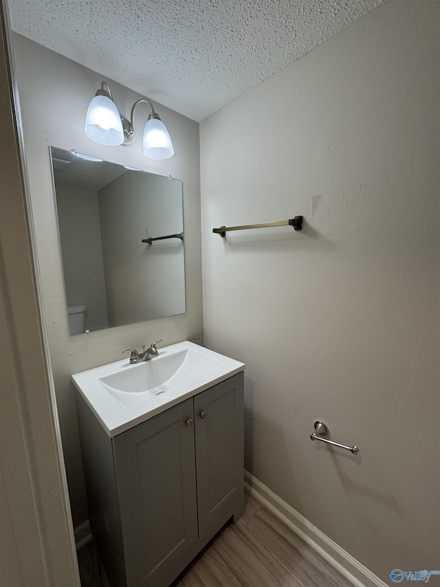 bathroom with hardwood / wood-style flooring, vanity, toilet, and a textured ceiling