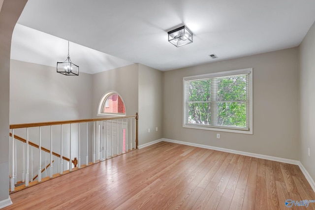 unfurnished room featuring wood-type flooring, baseboards, a notable chandelier, and a healthy amount of sunlight