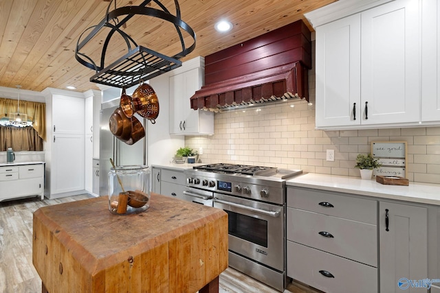 kitchen featuring custom exhaust hood, high end stainless steel range, light wood finished floors, wooden ceiling, and recessed lighting