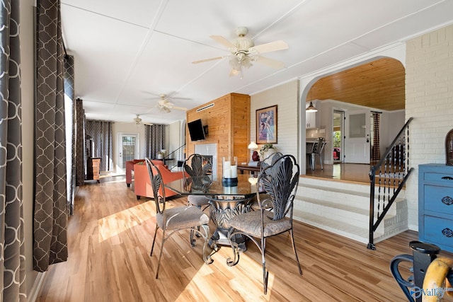 dining area featuring stairs, light wood-type flooring, ceiling fan, arched walkways, and wood walls
