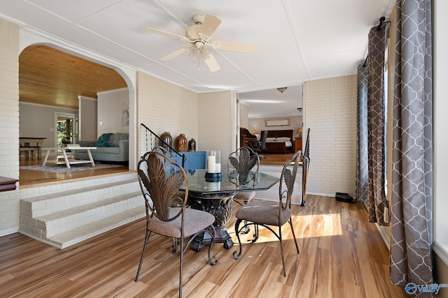 dining room featuring brick wall, a ceiling fan, wood finished floors, and arched walkways