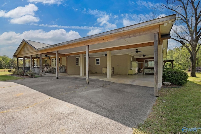 back of house with ceiling fan, an attached carport, aphalt driveway, and a yard