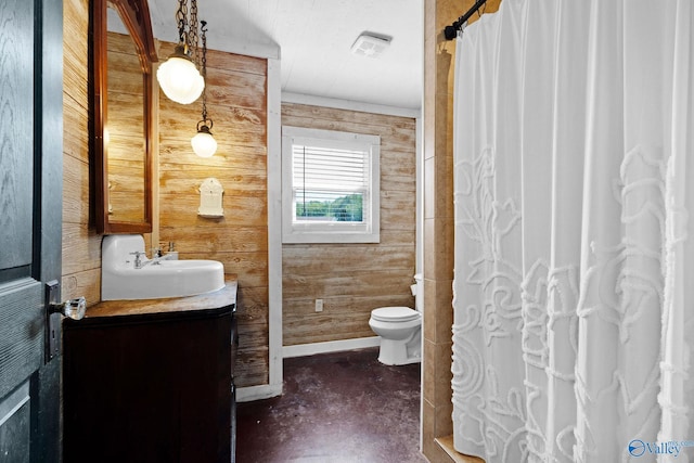 bathroom featuring wooden walls, toilet, vanity, baseboards, and finished concrete floors