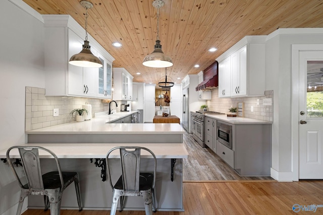 kitchen with stainless steel appliances, light countertops, a sink, wall chimney exhaust hood, and wood ceiling