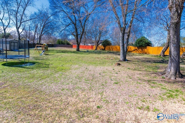 view of yard featuring a trampoline, an outbuilding, a playground, a storage unit, and a fenced backyard