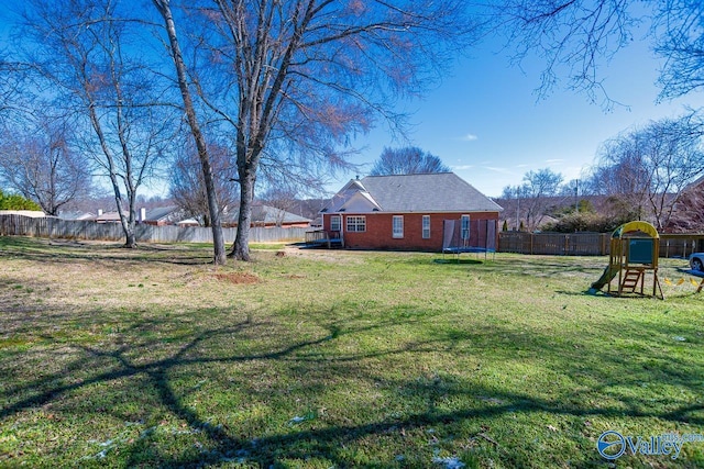 view of yard featuring a trampoline, a playground, and a fenced backyard