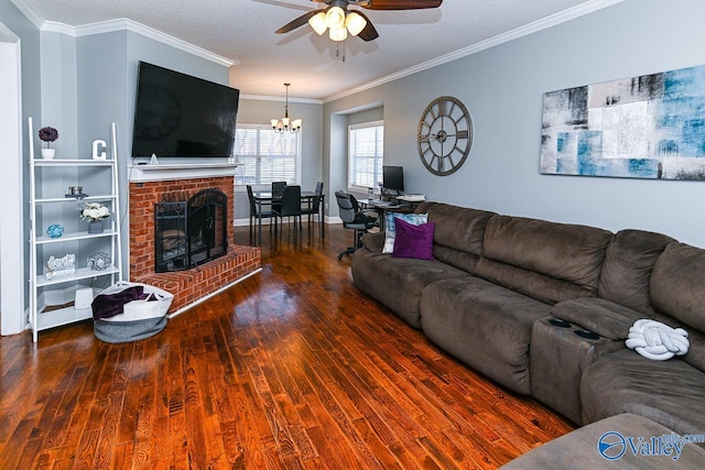 living area featuring crown molding, dark wood-type flooring, a brick fireplace, baseboards, and ceiling fan with notable chandelier