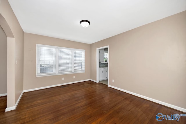 empty room featuring dark wood-style floors, arched walkways, and baseboards