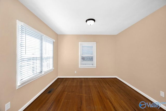 empty room featuring visible vents, baseboards, and dark wood-type flooring