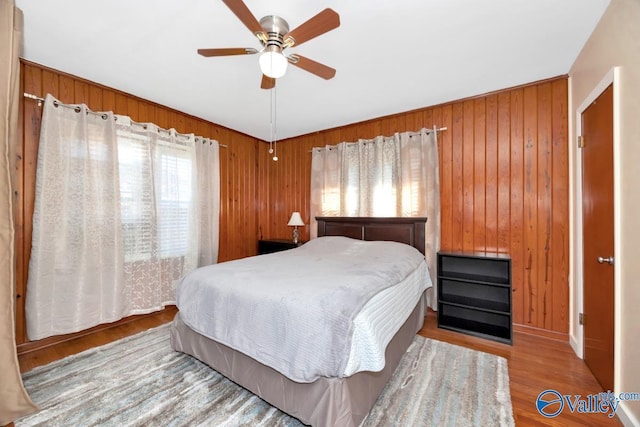 bedroom featuring ceiling fan, wood walls, and wood finished floors