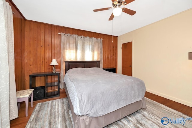 bedroom featuring ceiling fan, wooden walls, baseboards, and wood finished floors