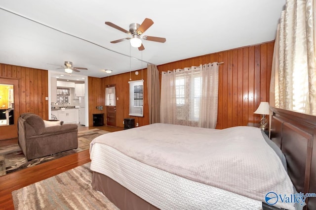 bedroom featuring a ceiling fan, wood walls, and wood finished floors