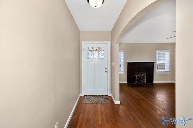 entryway with dark wood-style floors, a fireplace with flush hearth, arched walkways, and baseboards