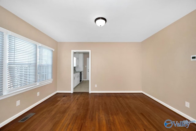 spare room featuring dark wood finished floors, visible vents, and baseboards