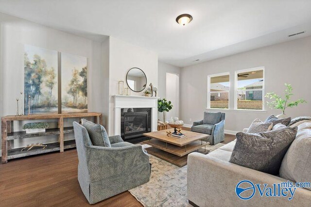 living area featuring wood finished floors, baseboards, a glass covered fireplace, and visible vents