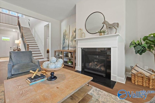 living room with baseboards, stairway, a glass covered fireplace, and wood finished floors