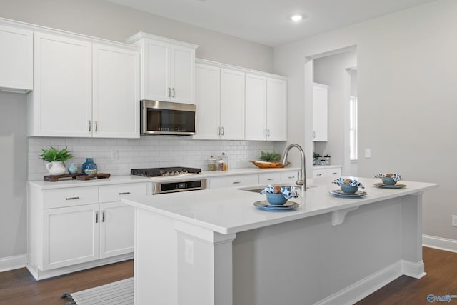 kitchen with dark wood finished floors, white cabinetry, a sink, stainless steel appliances, and decorative backsplash