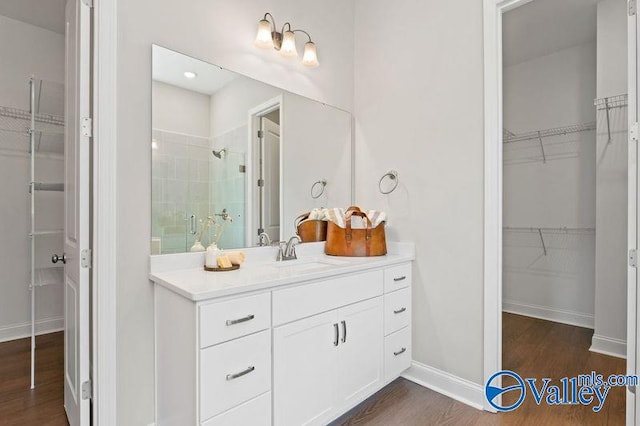 bathroom with vanity, baseboards, a stall shower, a walk in closet, and wood finished floors