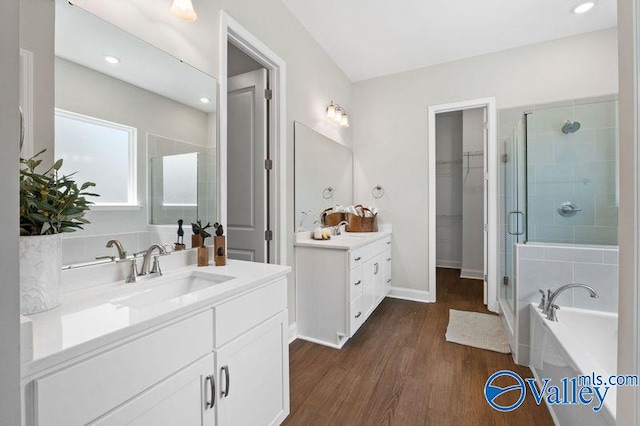 bathroom with a sink, wood finished floors, two vanities, a stall shower, and a garden tub