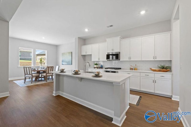 kitchen with tasteful backsplash, light countertops, stainless steel microwave, and white cabinetry