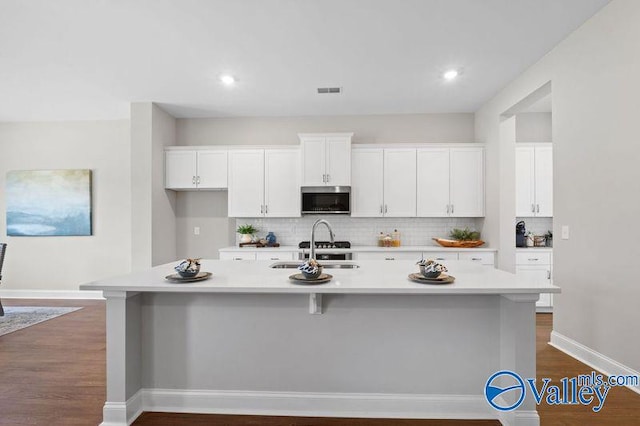 kitchen with white cabinetry, stainless steel microwave, light countertops, a sink, and decorative backsplash