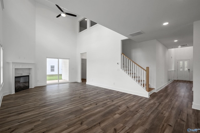 unfurnished living room with dark wood-type flooring, a premium fireplace, visible vents, a ceiling fan, and stairs