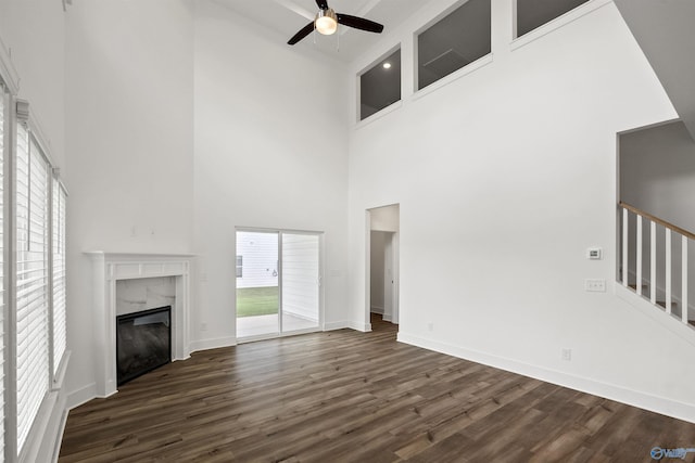 unfurnished living room featuring a fireplace, dark wood finished floors, ceiling fan, baseboards, and stairs