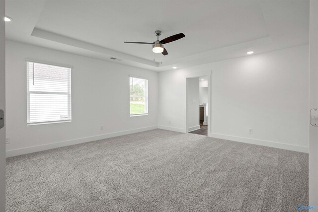 unfurnished room featuring carpet floors, a tray ceiling, a ceiling fan, and baseboards