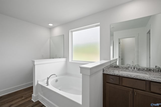 bathroom with a garden tub, vanity, baseboards, and wood finished floors